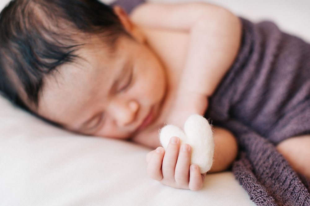 A sleeping child in a purple sweater holds a white object while resting peacefully on a bed.