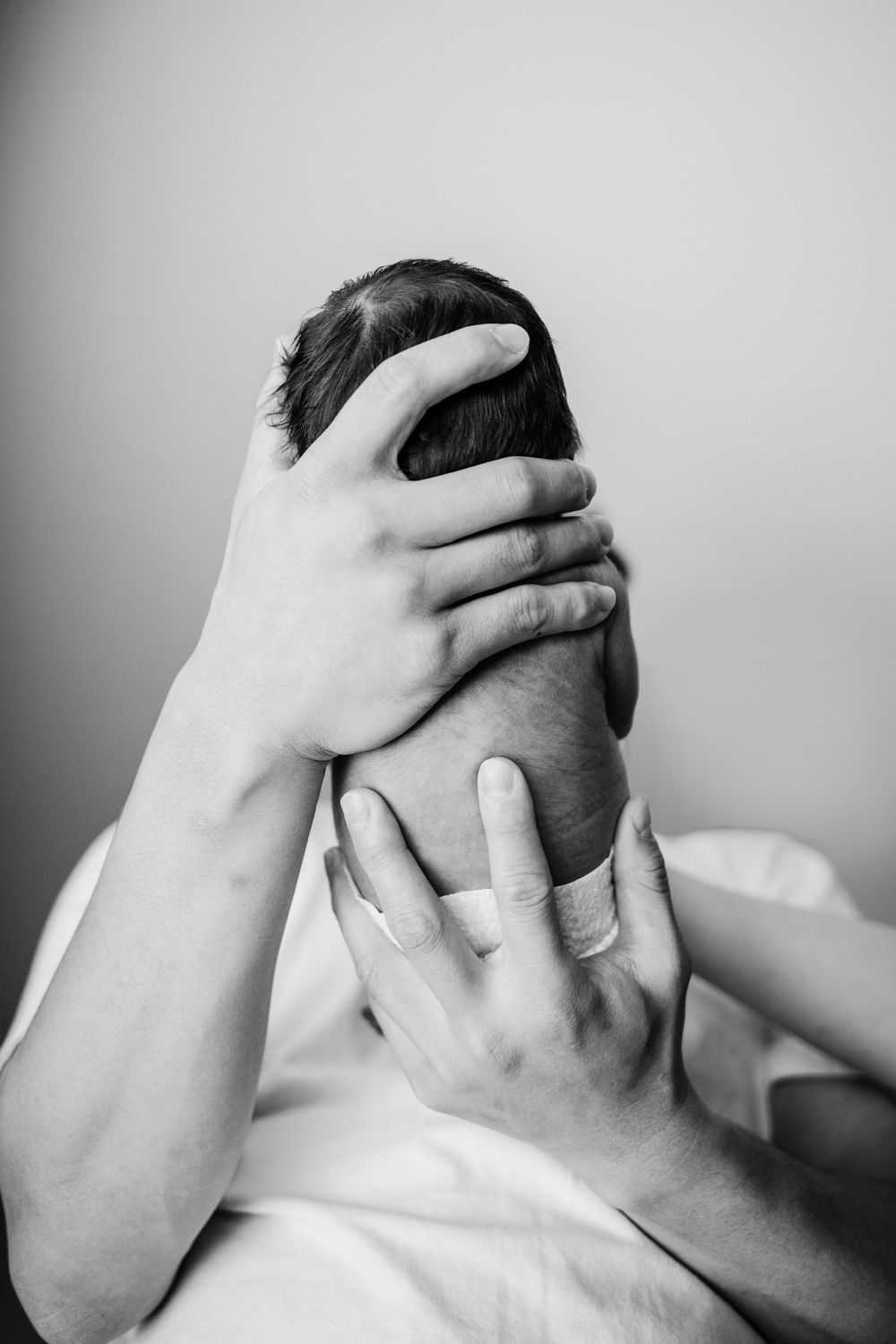 Hands grasping head in distress pose against gray background, artistic black and white portrait.