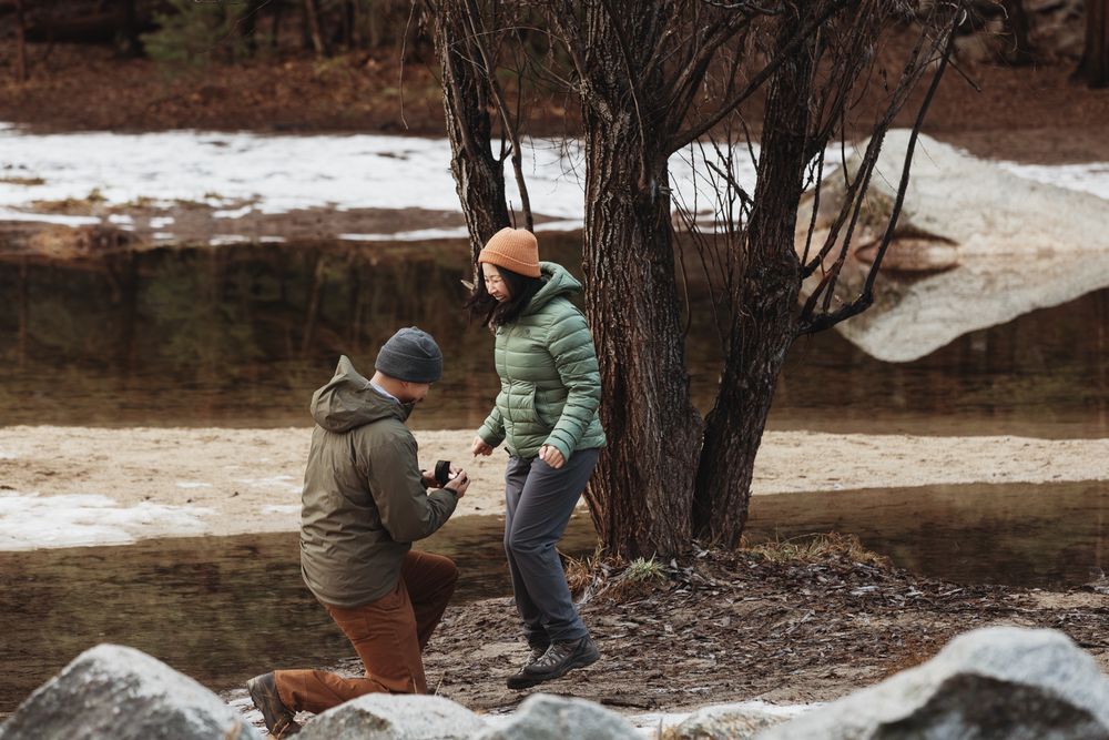A winter proposal scene with melting snow and bare trees near a stream on a cold day.