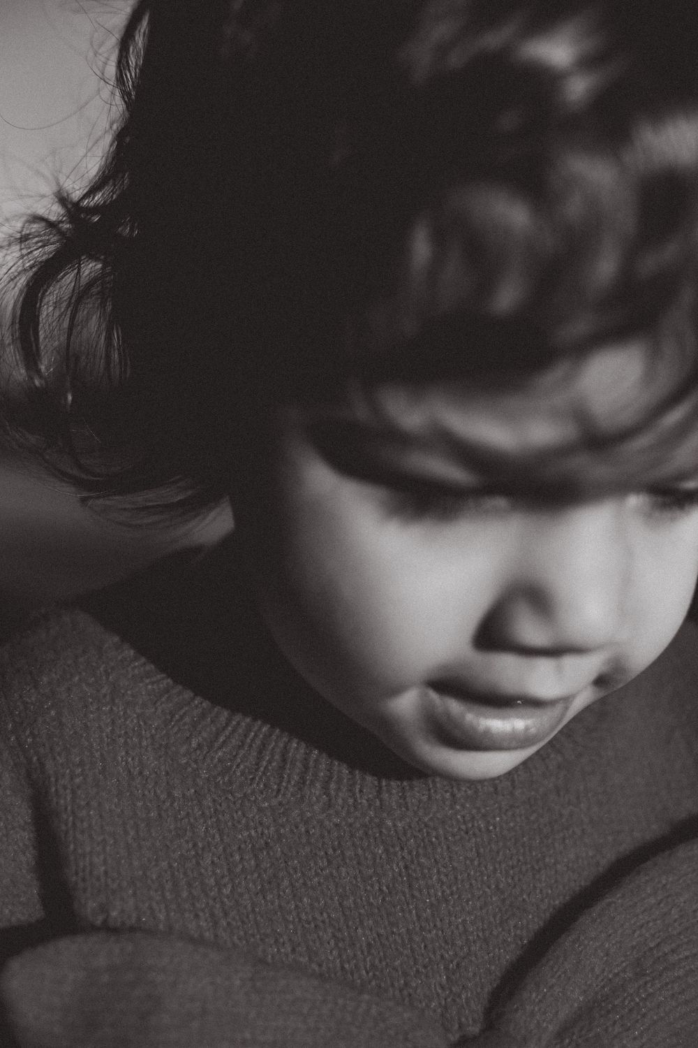 Artistic black and white portrait in dramatic lighting showing downward gaze while wearing a knit sweater.