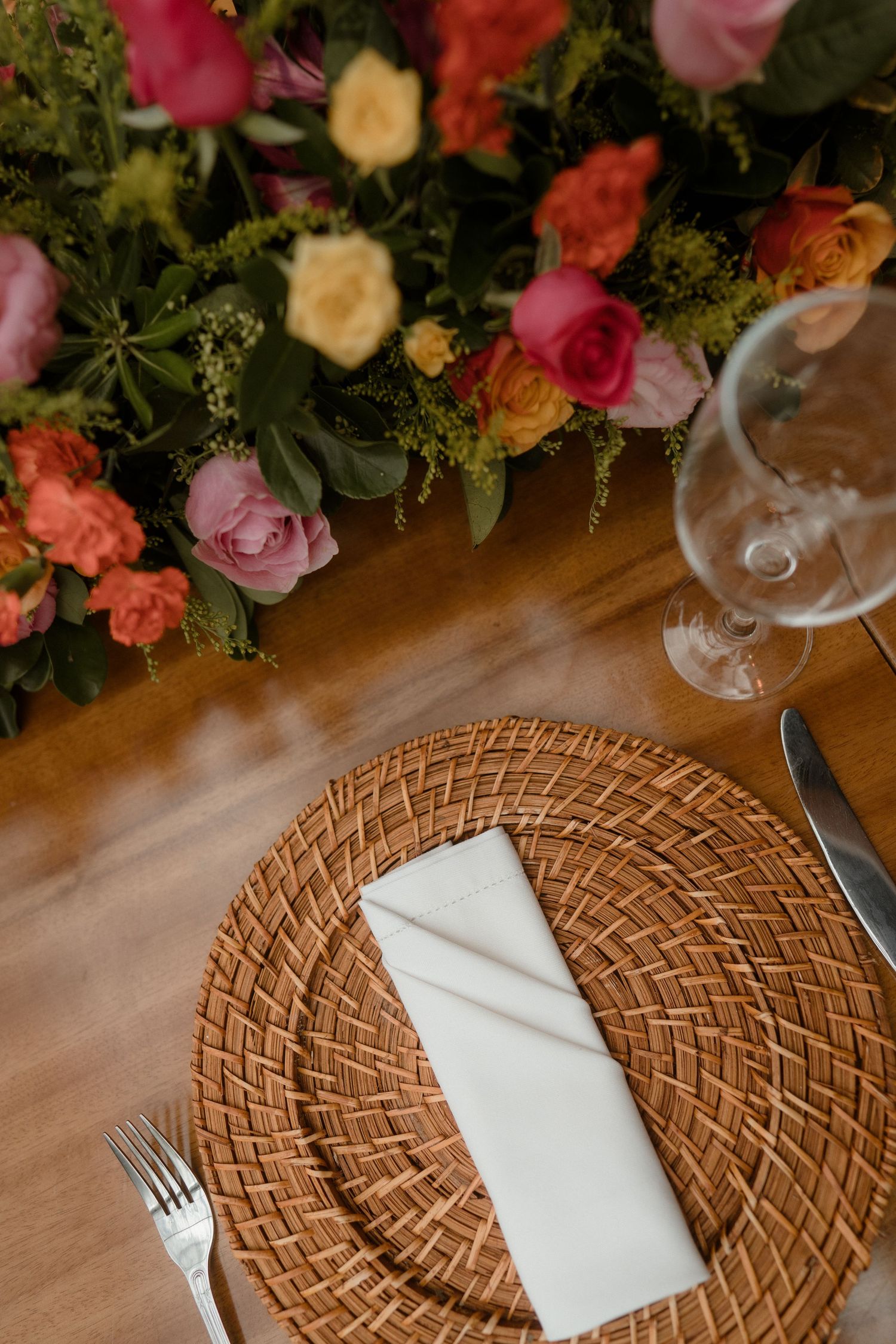 Table setting with woven charger plates and white napkins accented by pink and coral florals.