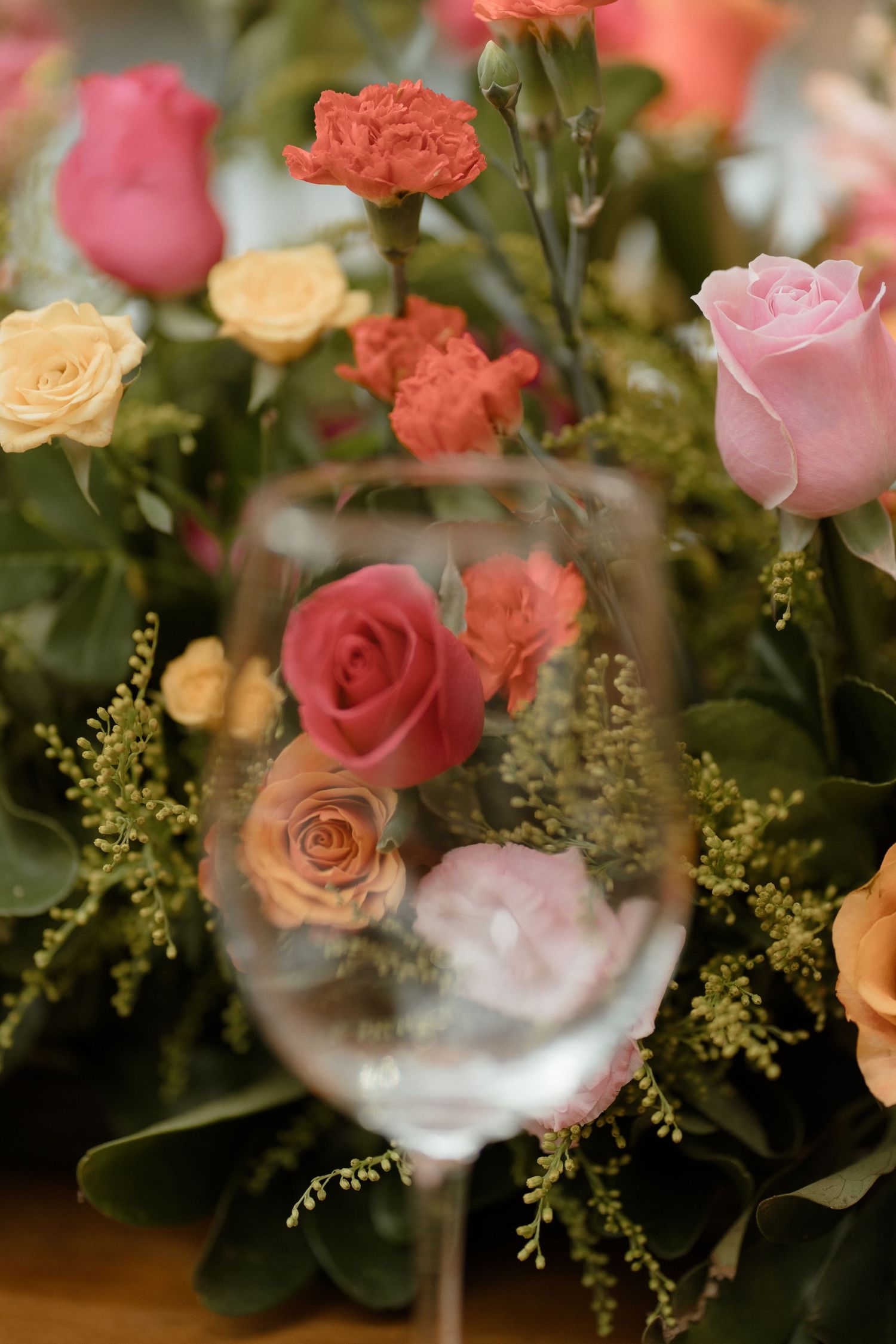 Close-up of coral, pink and peach roses with delicate greenery in a floral arrangement.