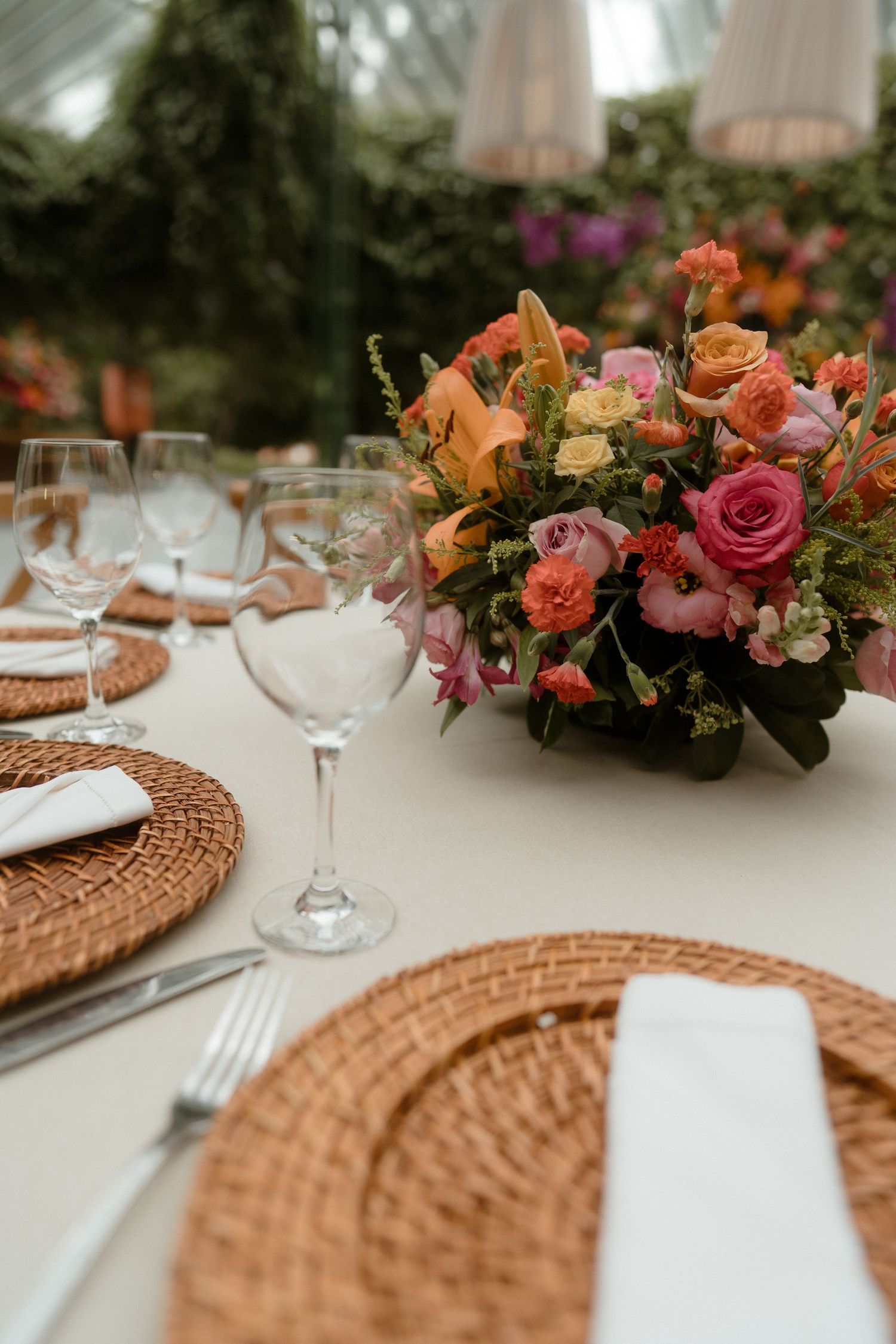 Elegant table setting with wicker chargers and colorful floral centerpiece featuring pink and orange roses.