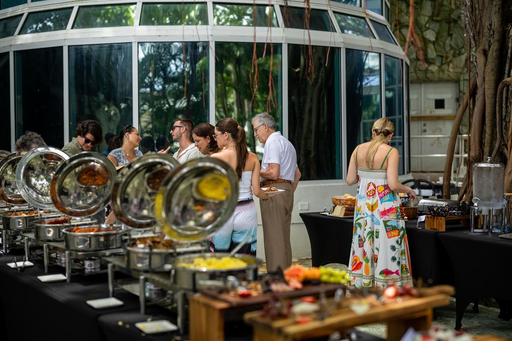 Buffet setup at an outdoor event with chafing dishes and serving stations under a glass-covered venue area.