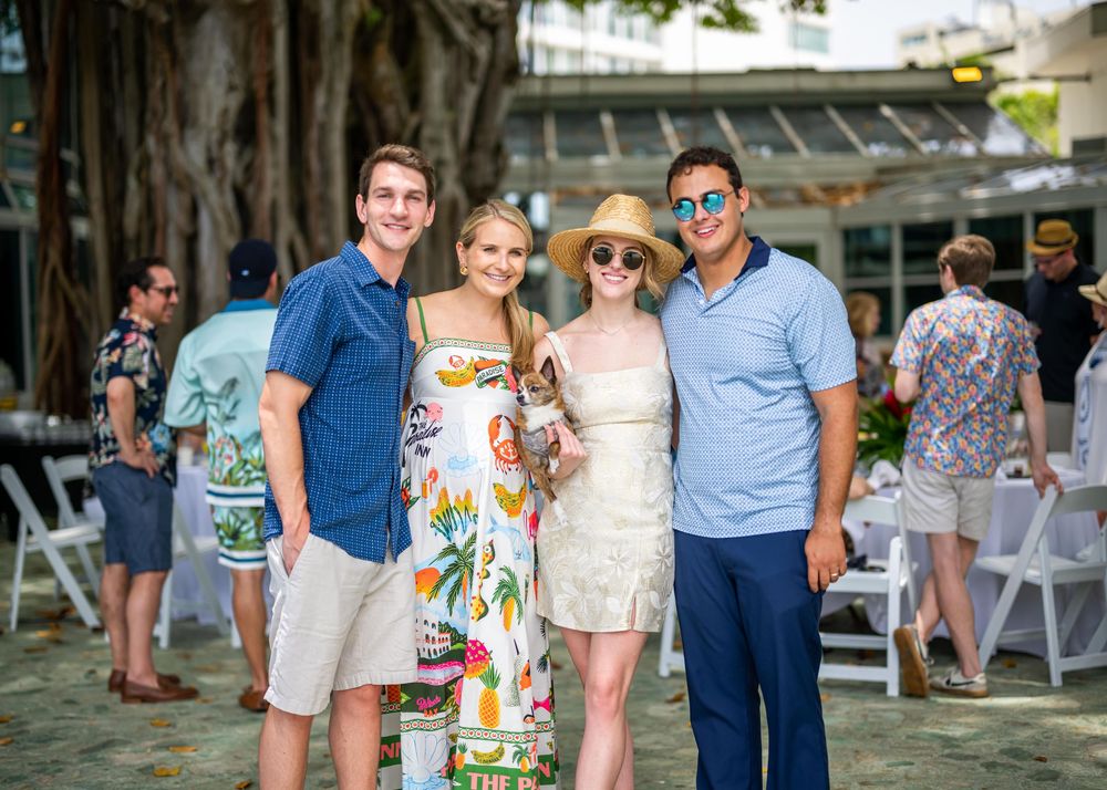 A group of friends in summer attire gathered outside at an outdoor venue with folding chairs visible in the background.