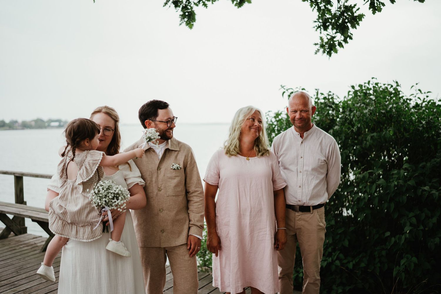 Two couples enjoy a warm moment together on a waterfront boardwalk surrounded by lush greenery.