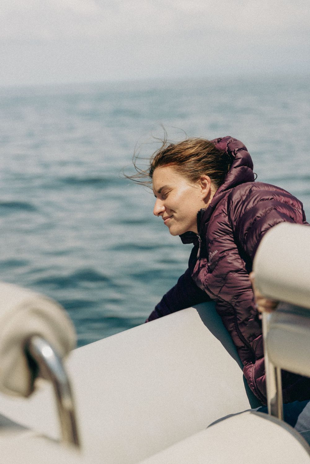 Person in purple jacket leans against the side of a boat while looking at the sea.