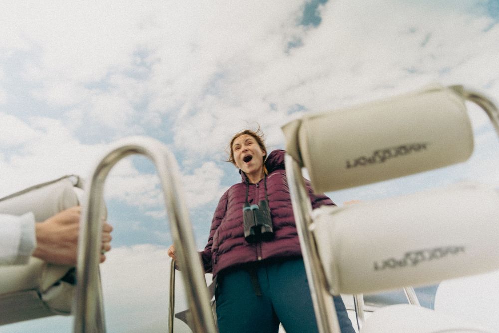 A person in a purple puffer jacket stands near boat equipment against a cloudy sky.