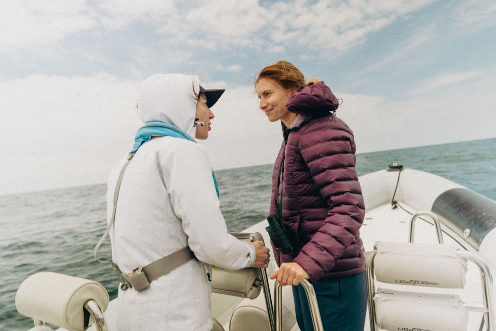 Two people chatting and laughing while standing on a boat deck at sea.
