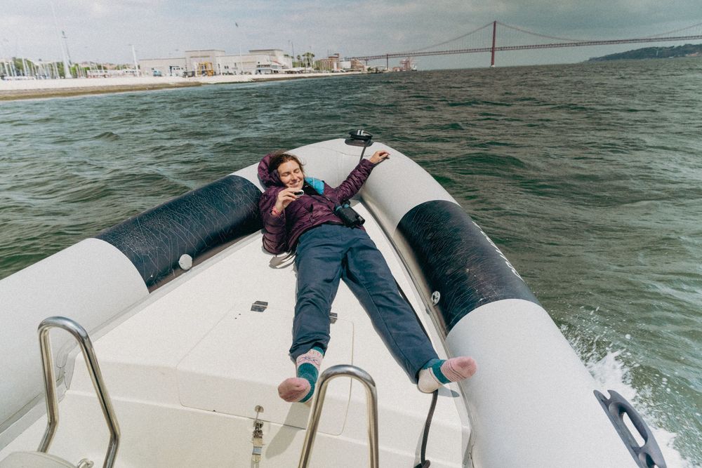 Person lounges across inflatable pontoons on speedboat while cruising through choppy ocean waters near coastline.