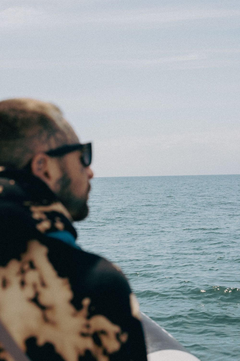 Person wearing sunglasses gazes at the ocean horizon from a boat on a cloudy day.