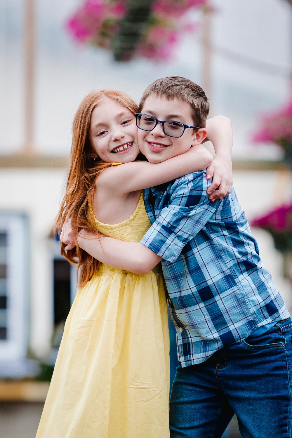Two children sharing a joyful hug and laughing together, one wearing a yellow dress and one in a blue plaid shirt.