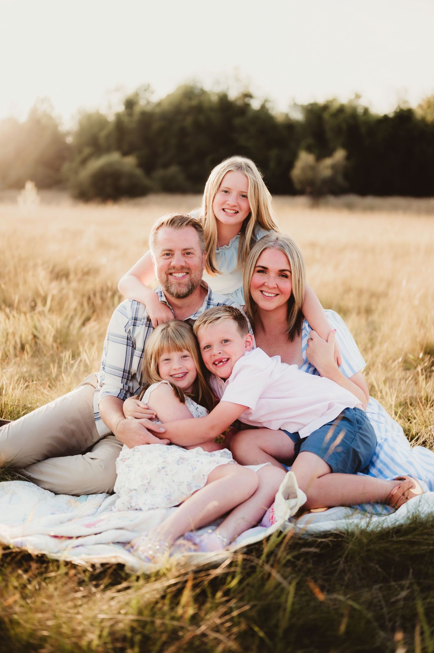 A family sits together on a blanket in a golden wheat field during sunset.