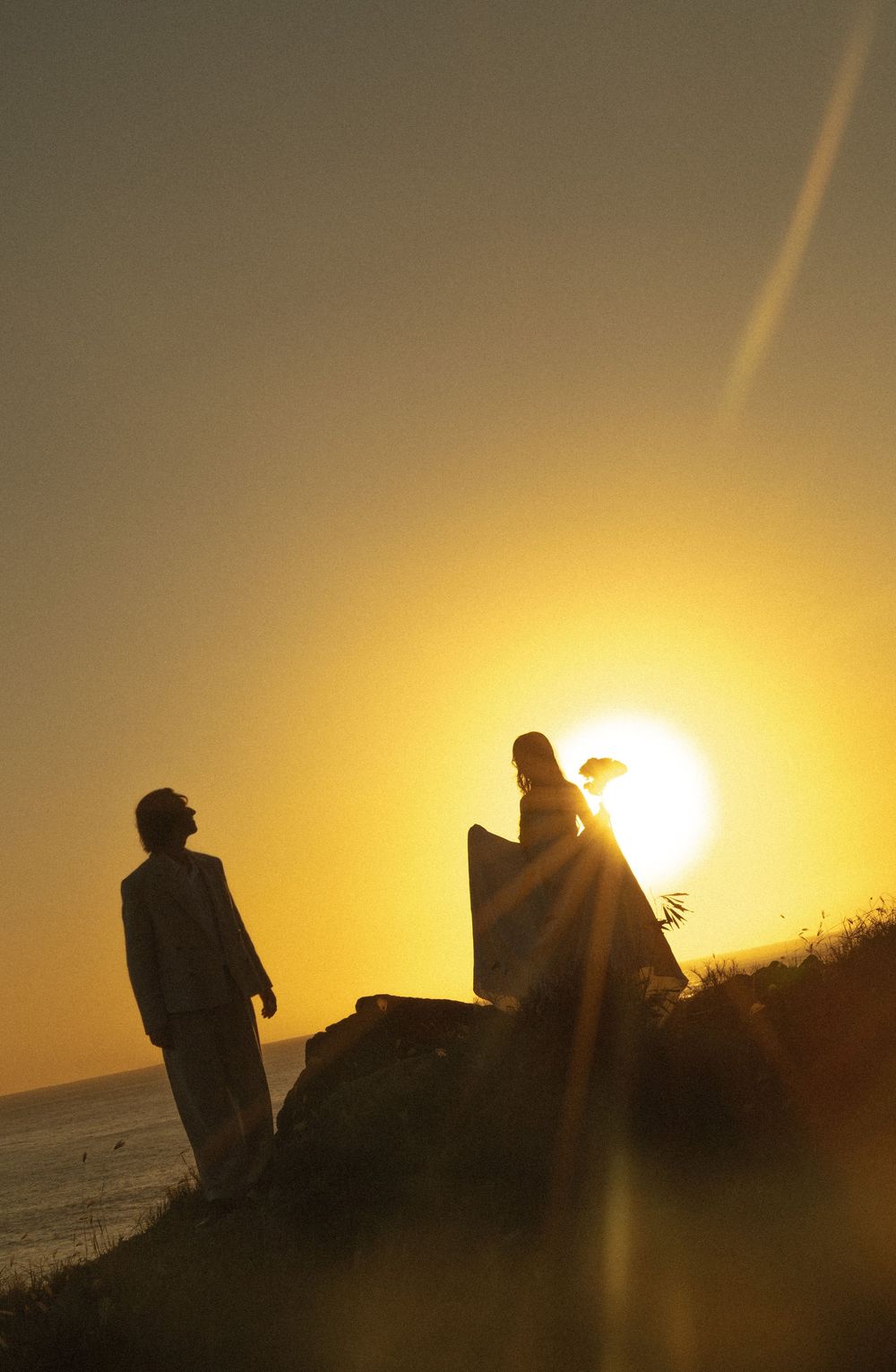 Two silhouetted figures stand on a hilltop against a dramatic golden sunset creating a powerful backlit composition.