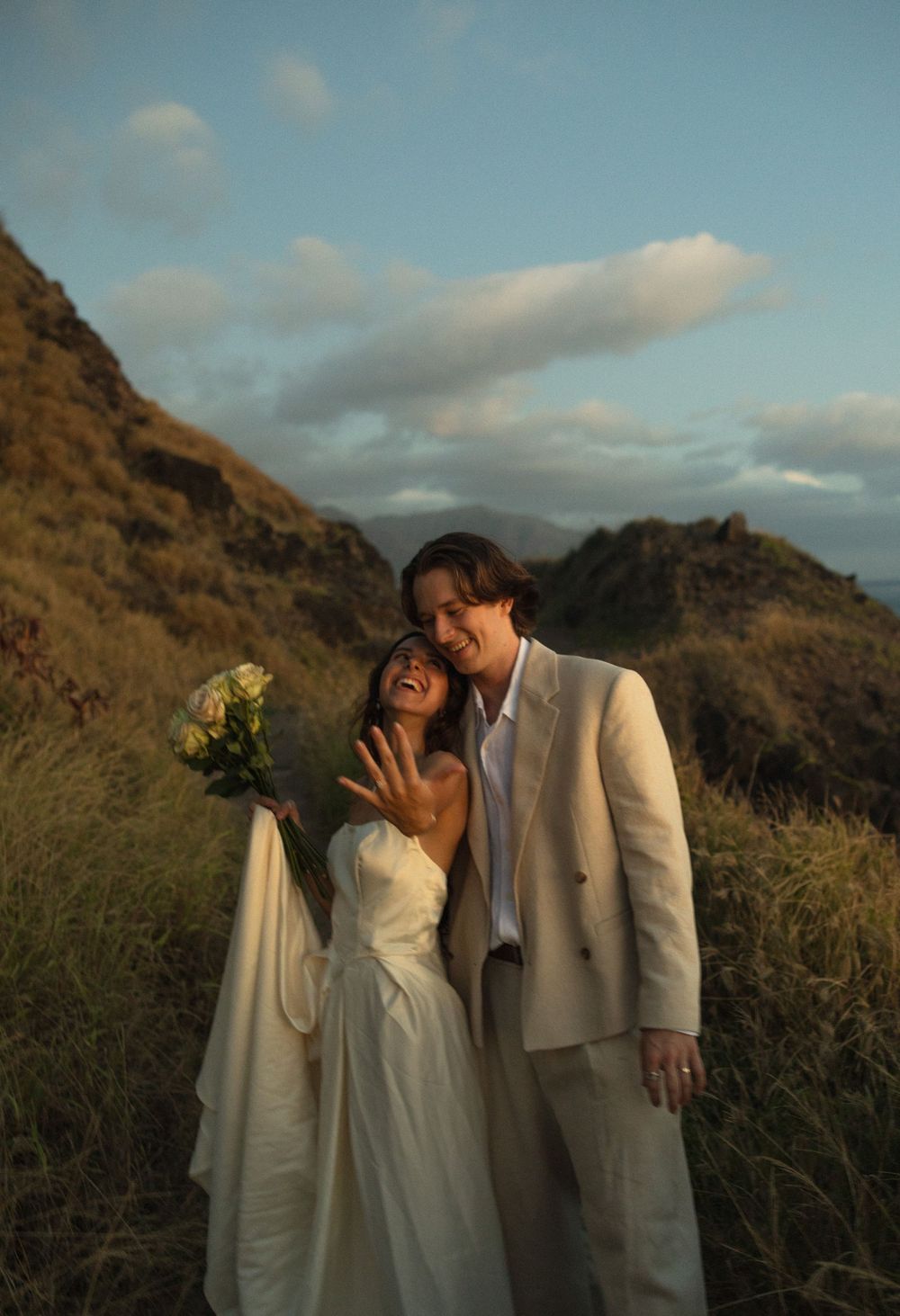 A couple in wedding attire share an intimate moment against a mountainous backdrop at golden hour.