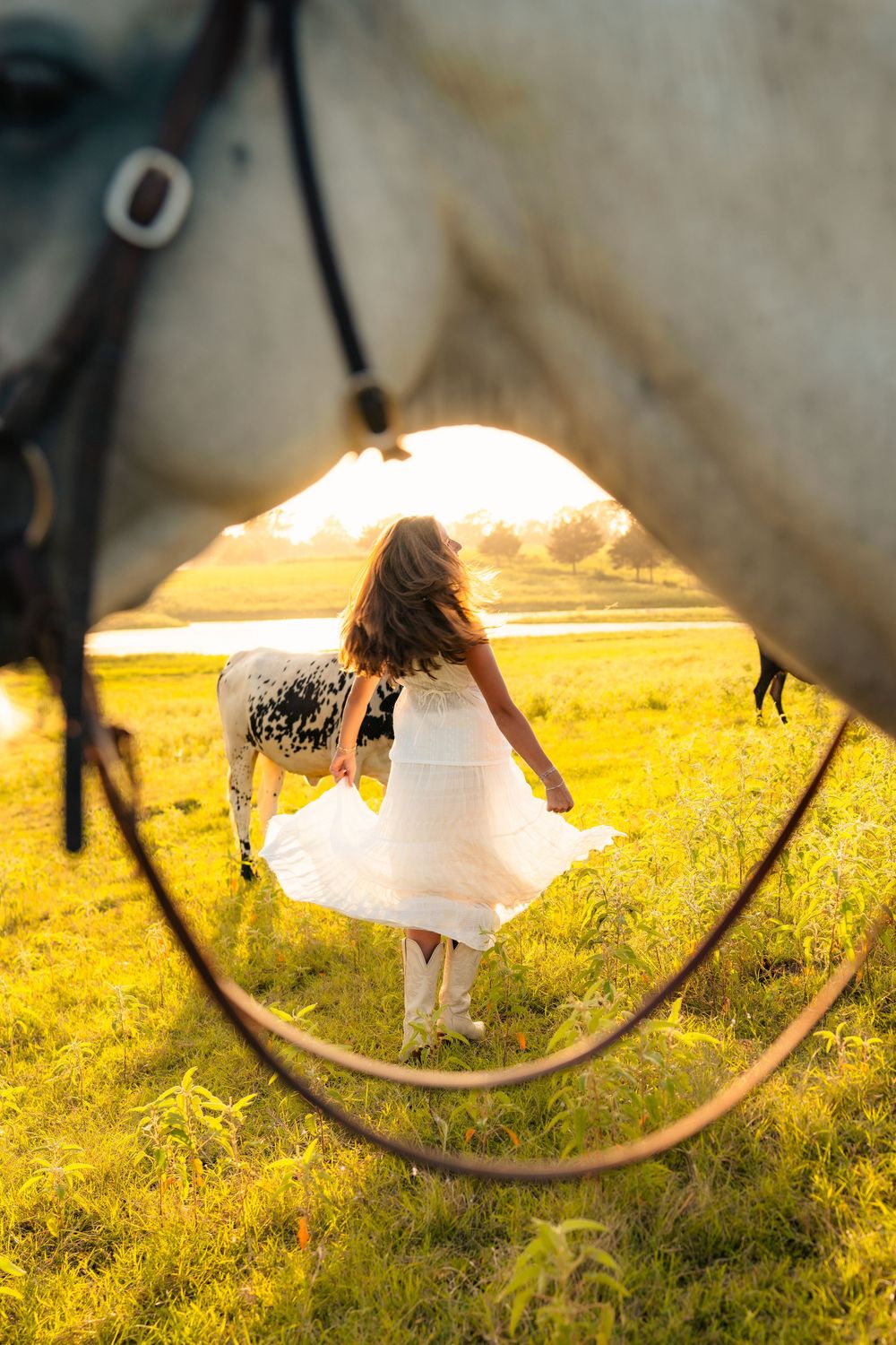Creative mirror reflection captures a figure in a white dress twirling in a golden sunlit field at sunset.