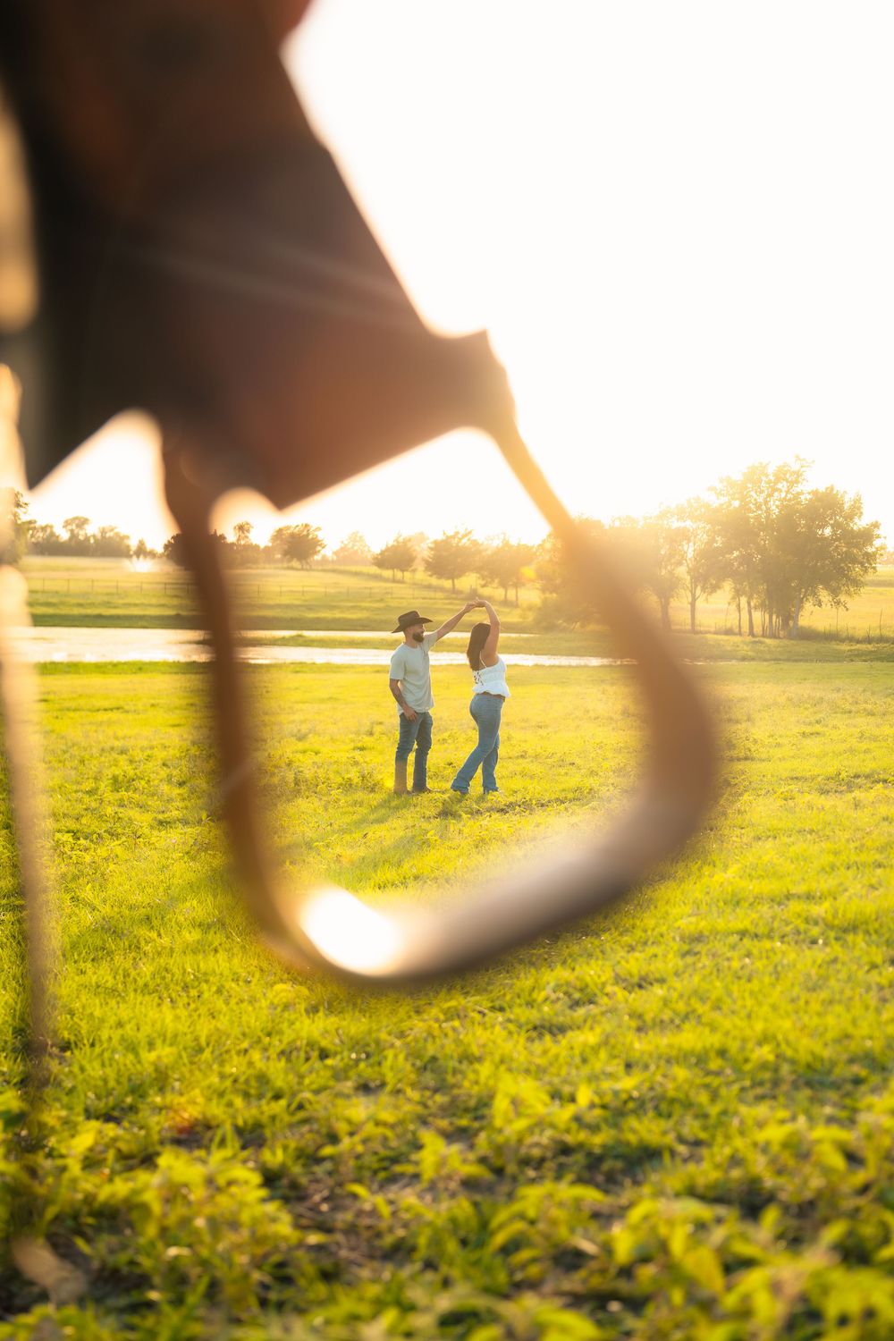 Two people standing in a grassy field at sunset, viewed through a guitar string silhouette in the foreground.