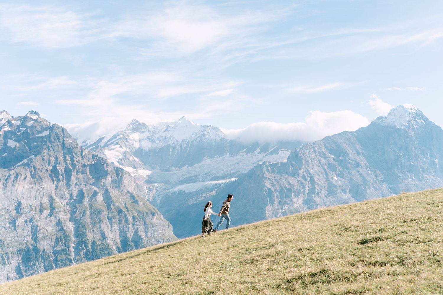 Two silhouettes stand near a pristine alpine lake surrounded by snow-covered mountains in Switzerland.