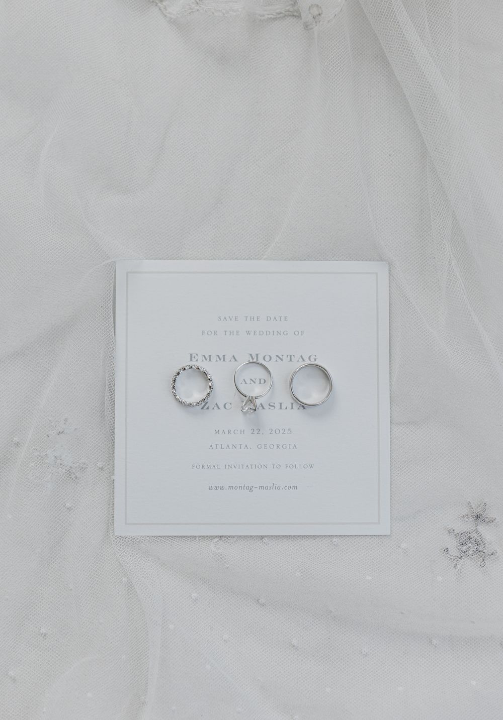 Three wedding rings arranged on a white invitation card against a soft tulle fabric background.