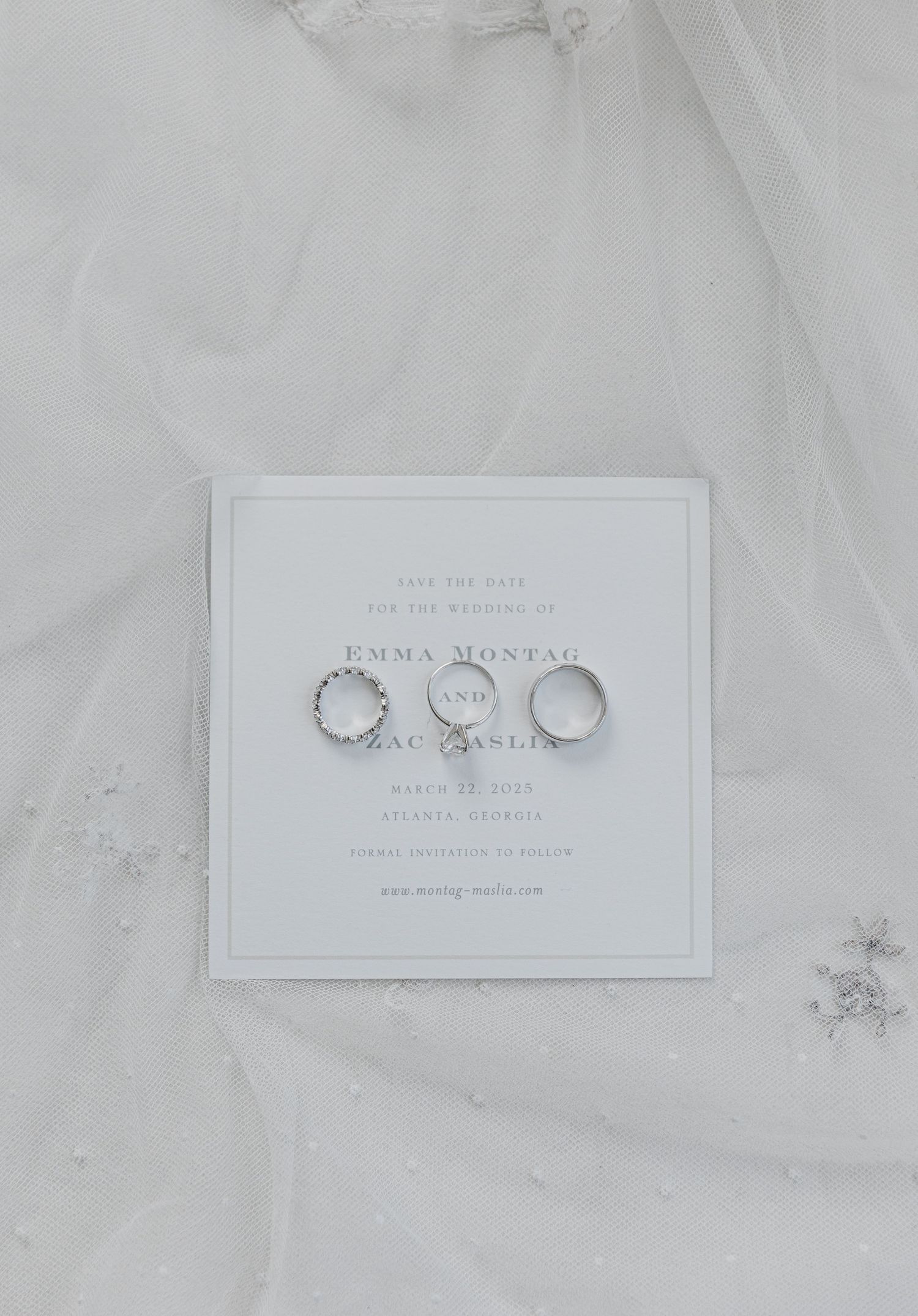 Three wedding rings arranged on a white invitation card against a soft tulle fabric background.