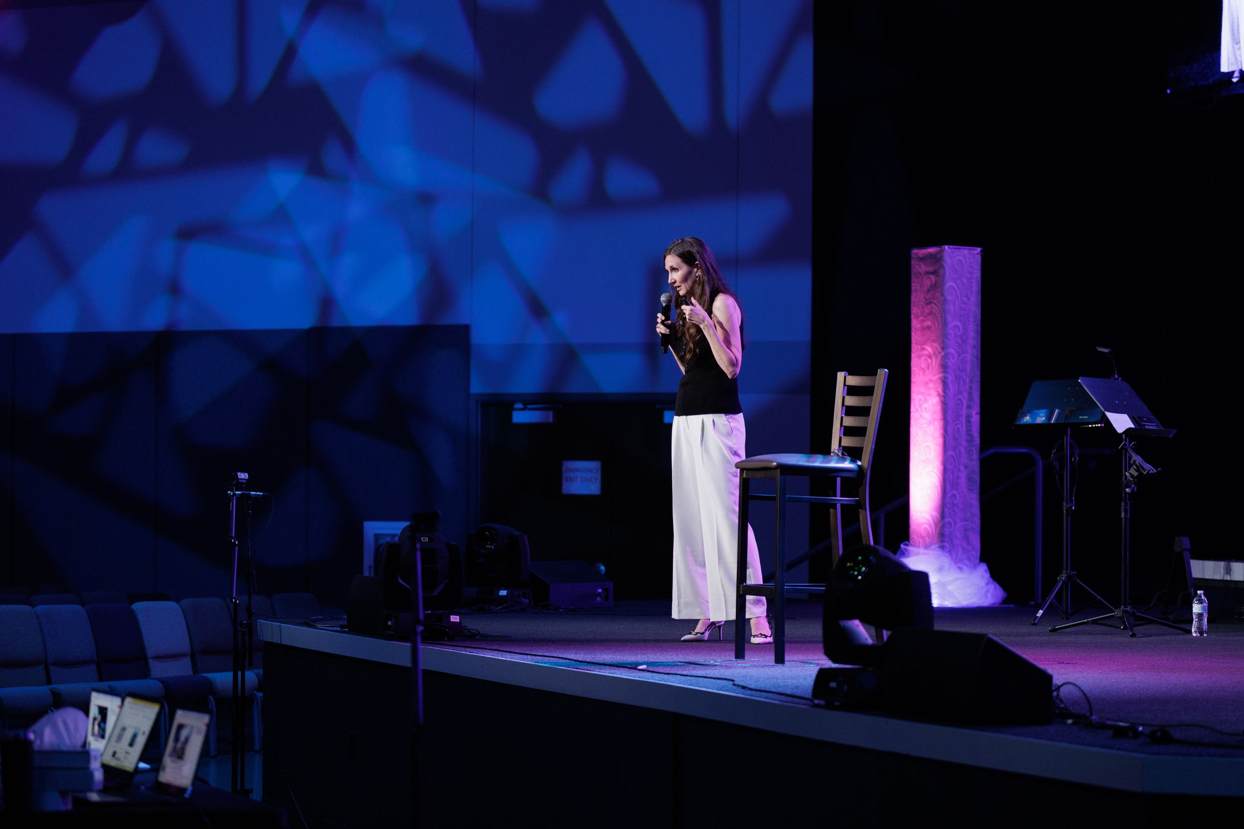 A performer stands on a dimly lit stage with blue lighting and geometric patterns projected in the background.