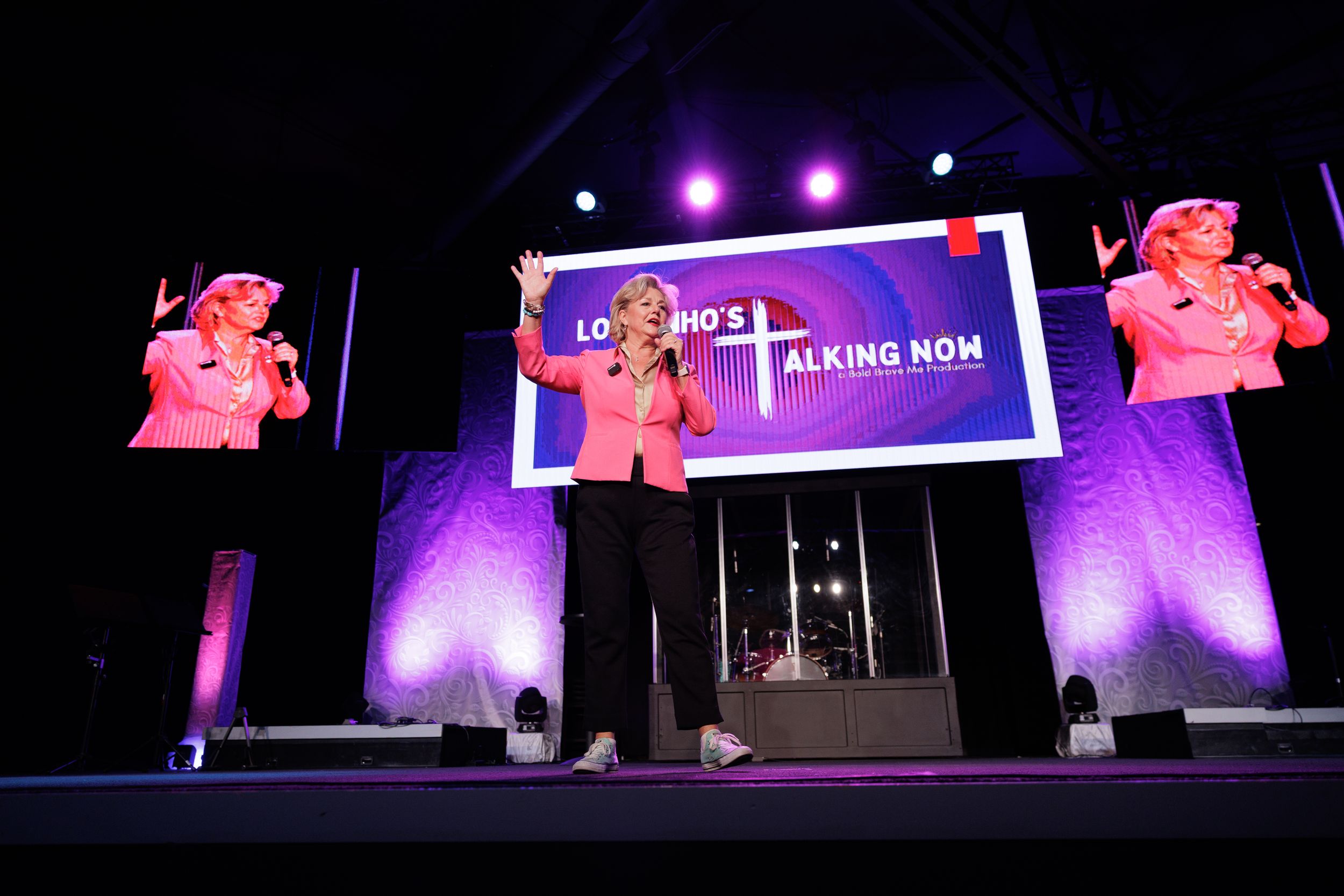 Stage performance setup with pink decorative elements and purple lighting featuring a central podium.