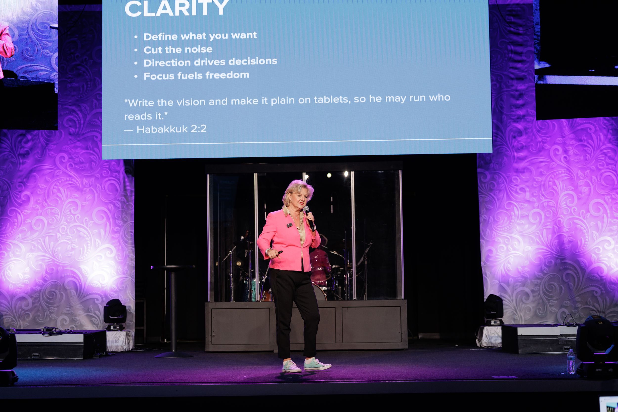 A presenter speaks on stage with a presentation slide about clarity displayed behind them.