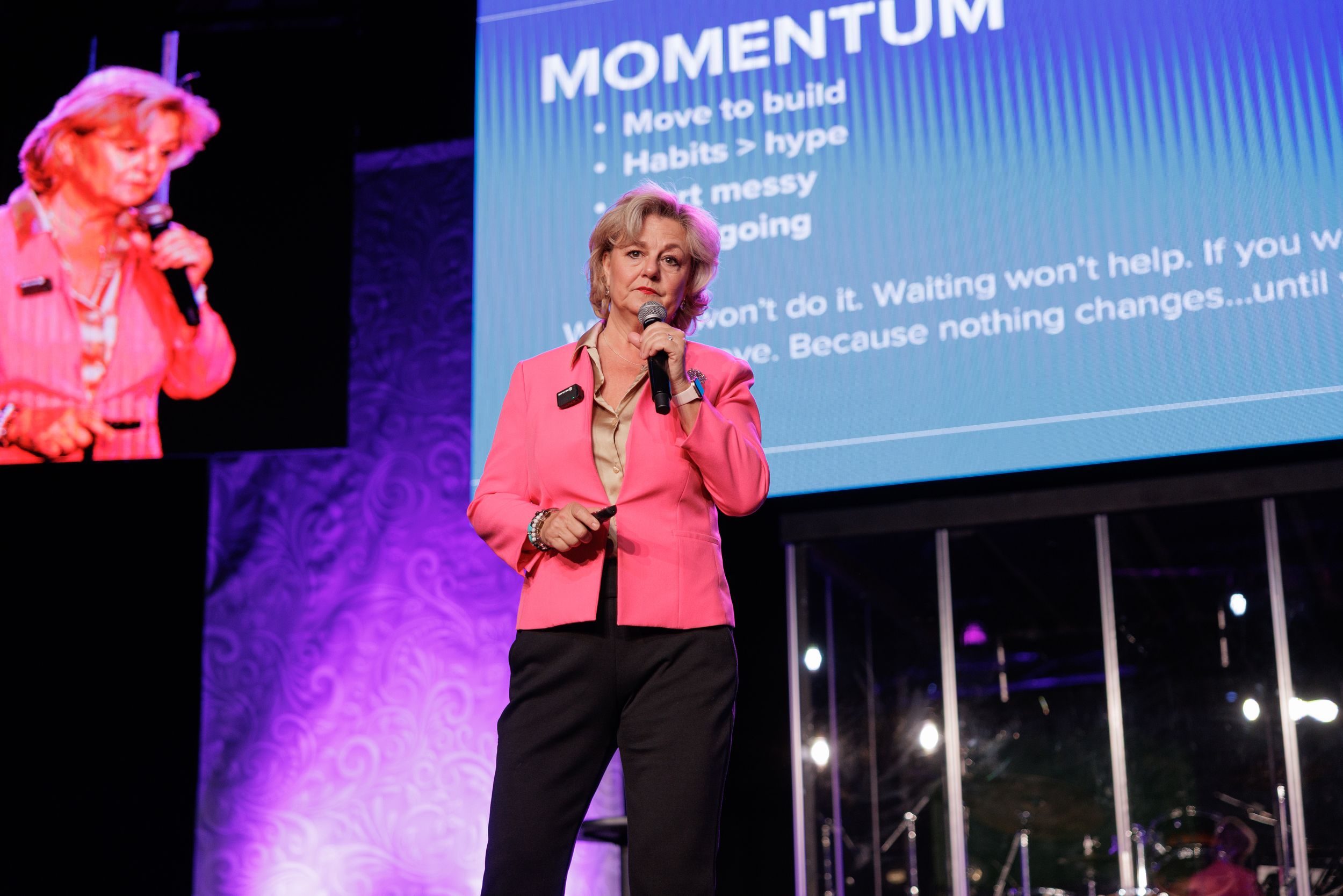 Conference presentation with momentum text displayed on screen and pink stage lighting.