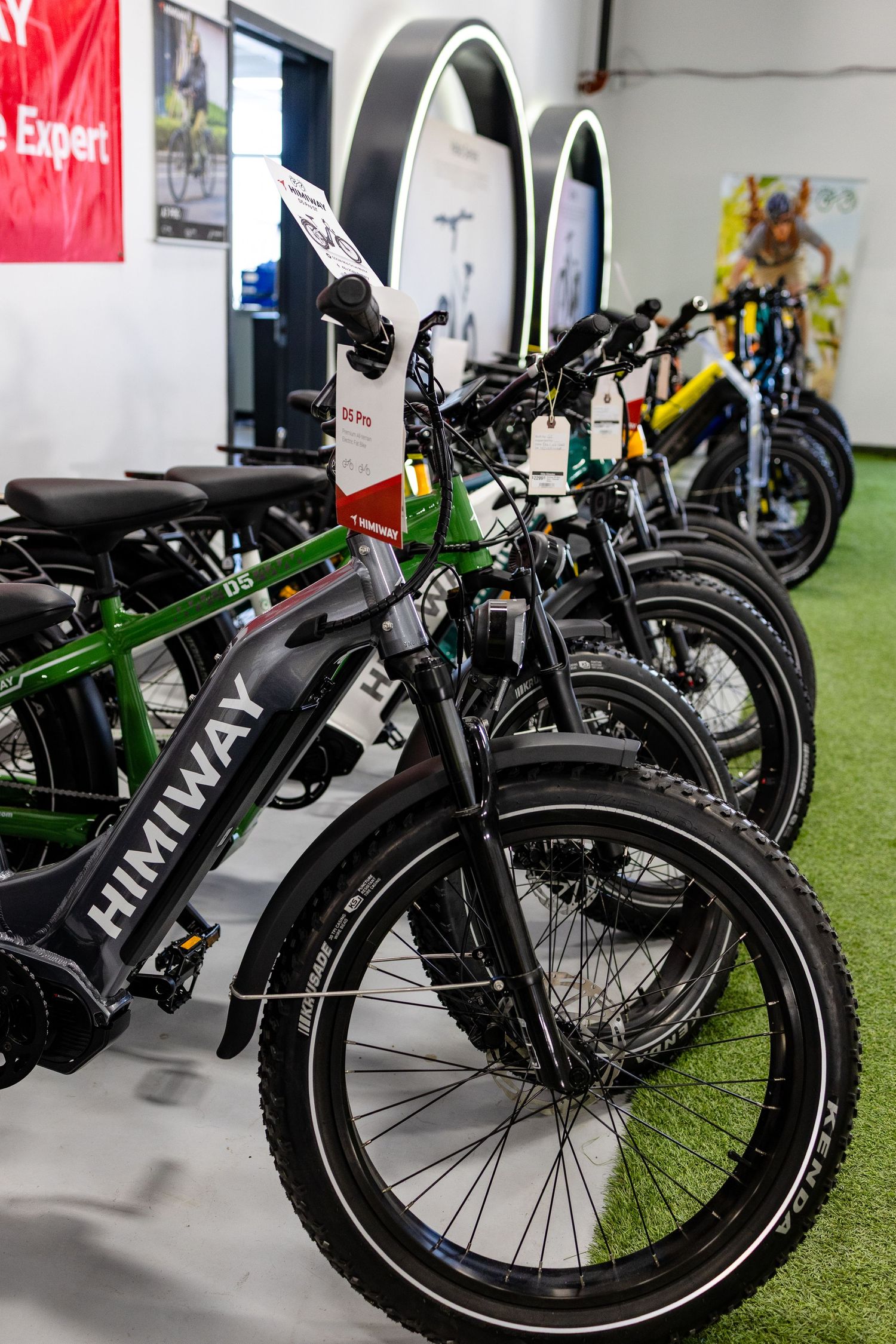 A lineup of black electric bicycles displayed in a showroom on artificial grass.