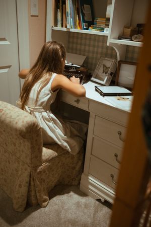 A person sits at a white desk with drawers in a cozy home office space.