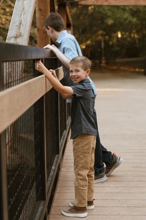 A child in khaki shorts and dark shirt plays on a wooden bridge railing on an autumn afternoon.