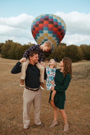 Family of four standing together outdoors in autumn forest with warm lighting during sunset photo shoot.