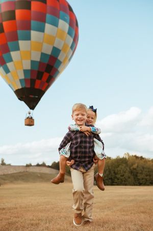 A colorful hot air balloon basket appears to float across a grassy field on a sunny day.