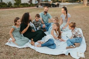 A family group sits together on a blanket outdoors enjoying quality time in a casual park setting.