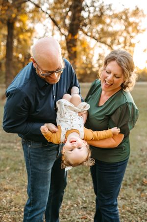 A joyful family shares a playful moment outside a storefront window with red accents in their outfits.