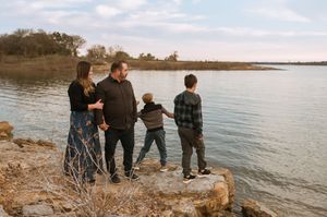 Family spending quality time together on a rocky shoreline during golden hour at a peaceful lake.