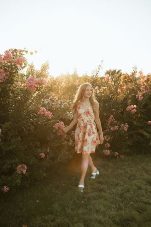A floral sundress twirls among blooming pink roses in a garden at golden hour sunset.
