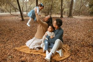 Family enjoying a fall day together on a blanket surrounded by autumn leaves in a park setting.