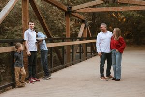 People gather on a rustic wooden bridge in a wooded outdoor setting during a social event.