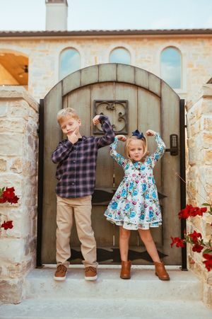 Children play and pose in front of a rustic stone house entrance with wooden doors.