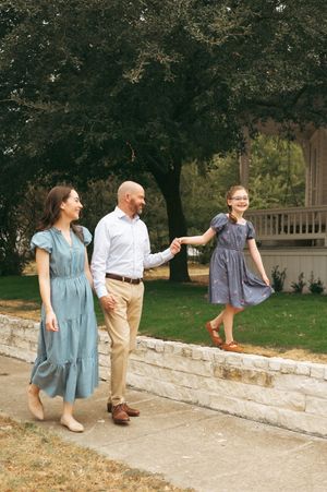 Family holding hands while walking through fallen autumn leaves in a park on a crisp fall day.