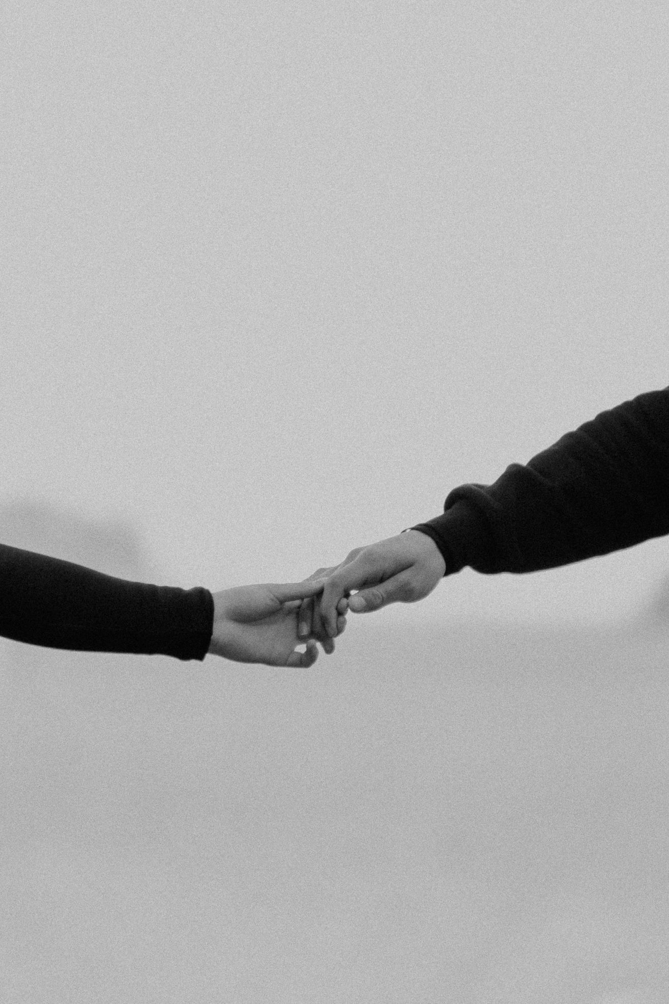 Two hands reaching towards each other against a gray background in a black and white artistic photograph.