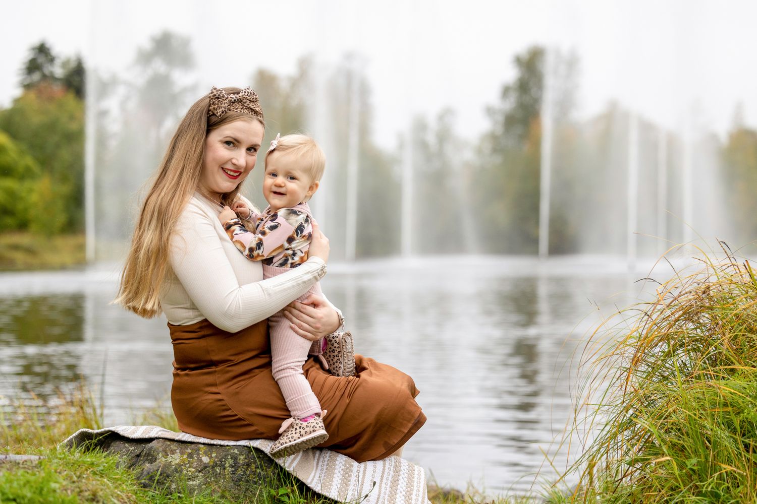 Äiti ja lapsi puistomaisemassa, taustalla suihkulähteitä.