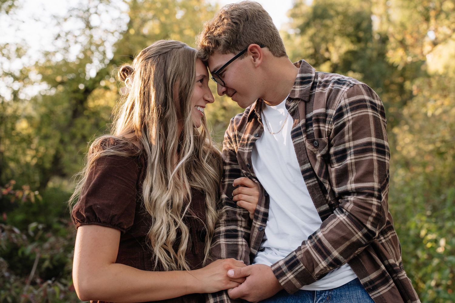 A couple shares romantic moments during a sunset engagement session in a field.