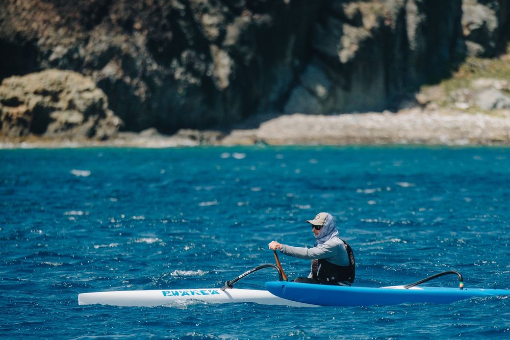A person kayaking on bright blue waters near rocky coastal cliffs on a sunny day.