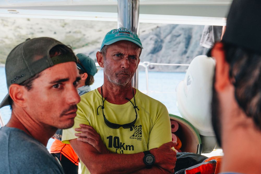 Three people having a conversation together on what appears to be a boat with mountains visible in the background.