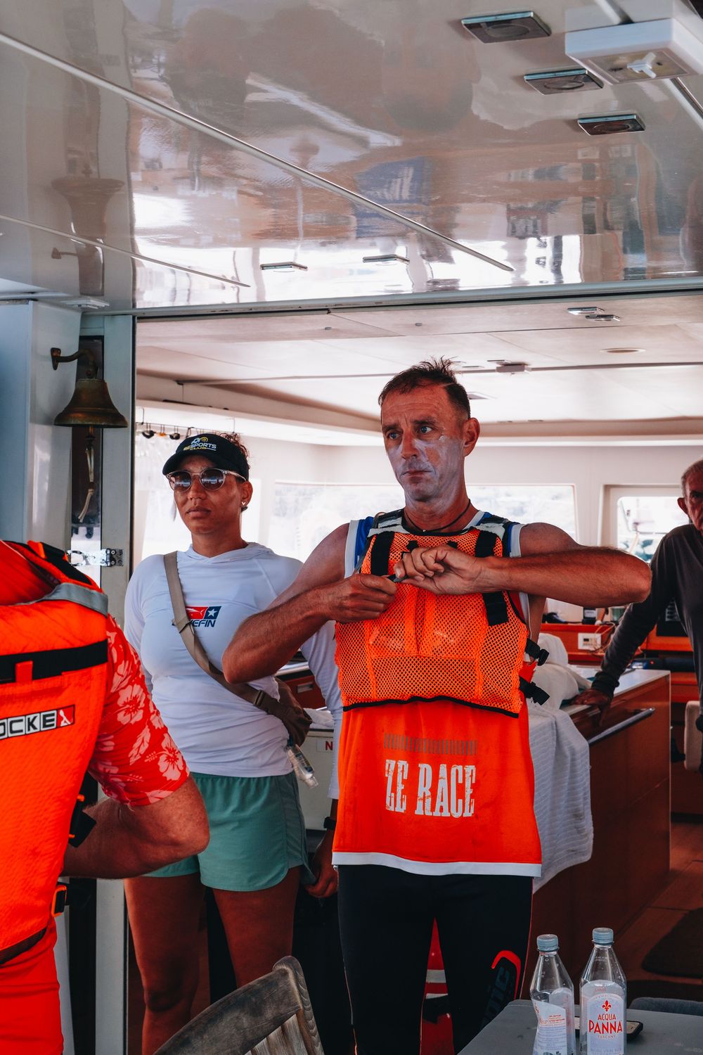 Two crew members help demonstrate proper life jacket safety procedures during a boat safety briefing.