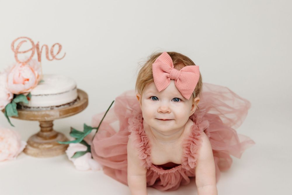 Baby in ruffled pink dress posing on white backdrop for first birthday photos.
