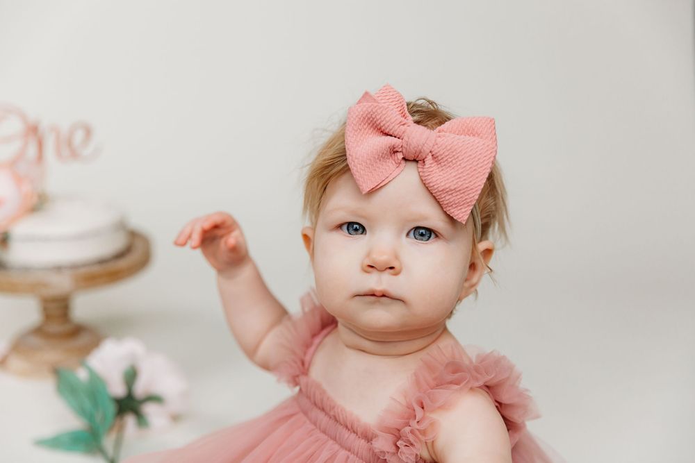 Close up of baby wearing pink bow and dress during first birthday photoshoot.