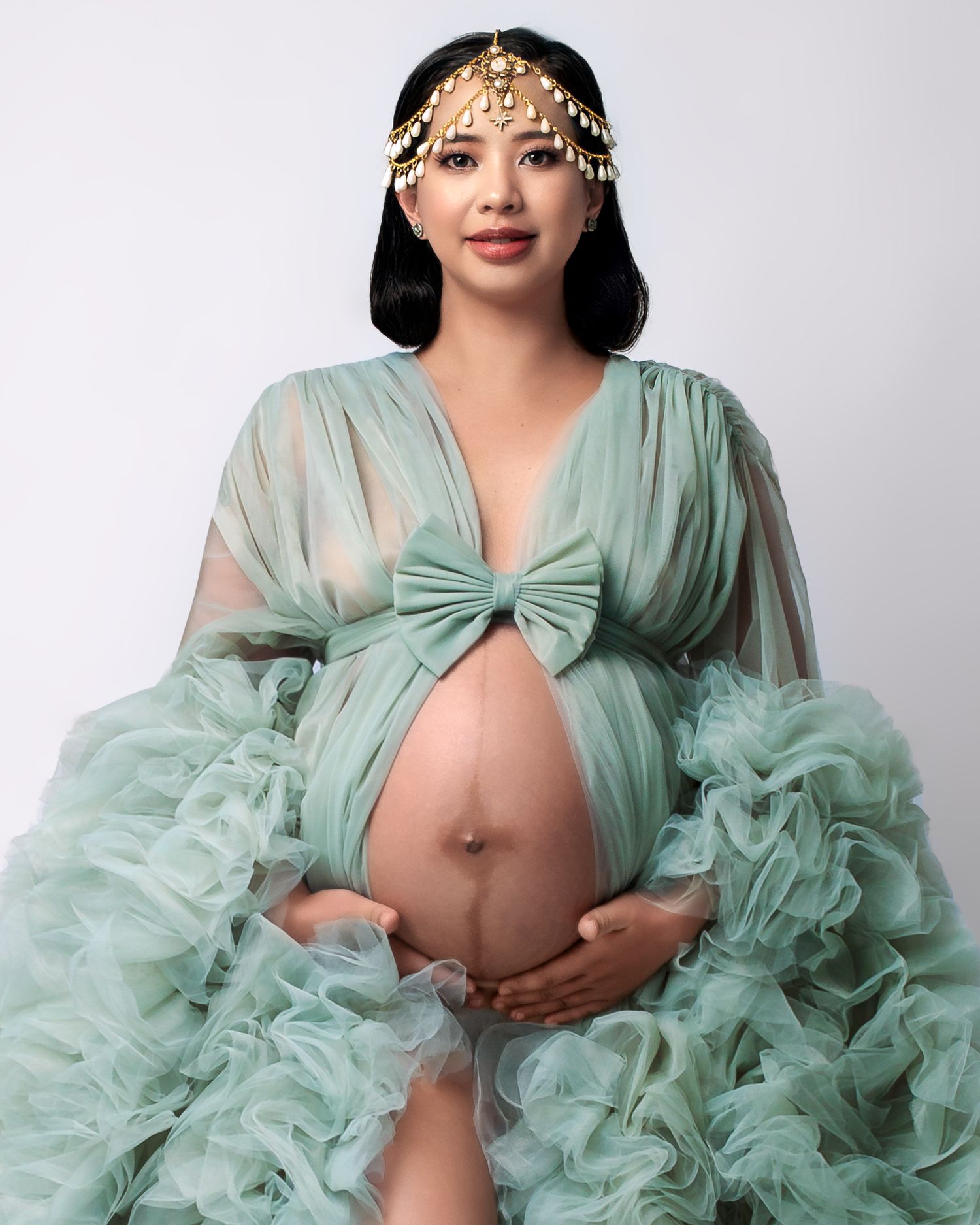 Studio maternity session: expectant mum in a simple sage robe and delicate gold and pearl drop headpiece.